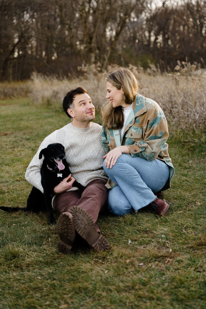 a couple sit together in a field with their pup during family portraits photography