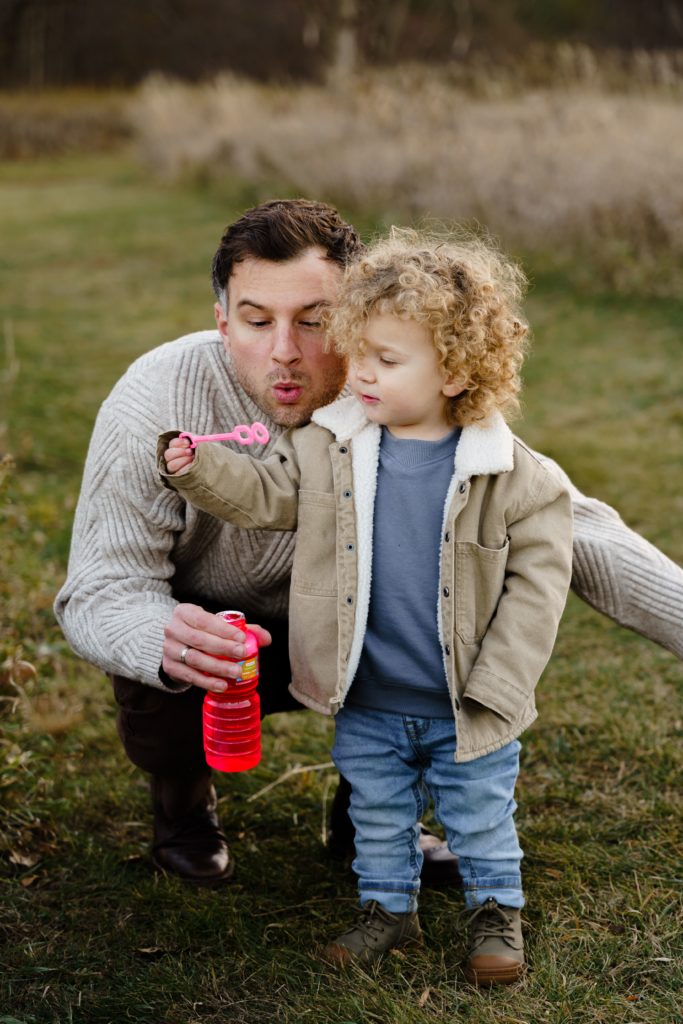 a dad blows bubbles with his son during family portraits