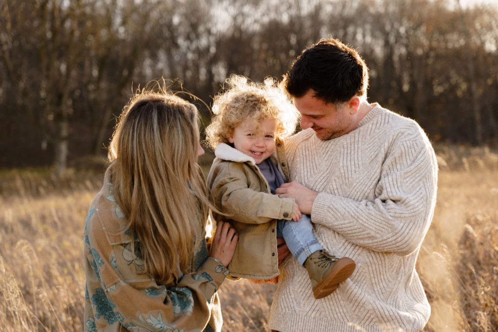 a father tickles his son while standing with his wife during family portraits