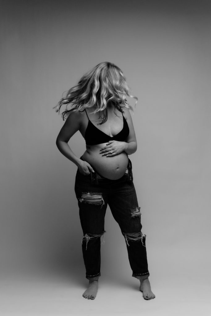 a motion blur portrait of an expecting mother shaking her head to create movement with her flowing blonde hair during her maternity photoshoot