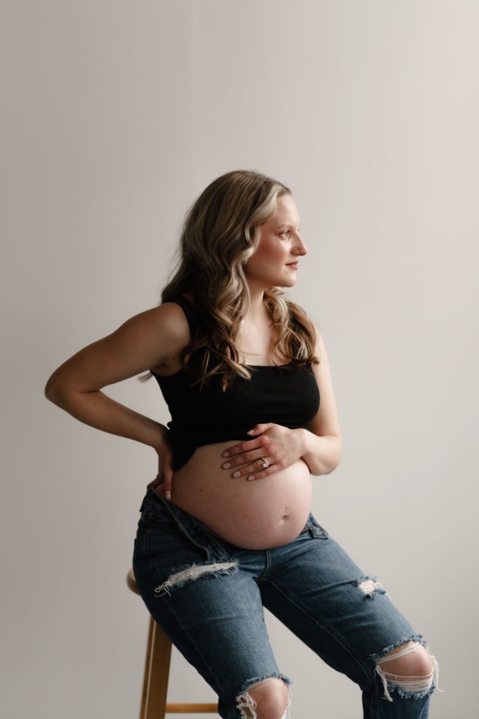 sitting on a stool wearing ripped jeans, chelsea sits for portraits with michigan maternity photographer