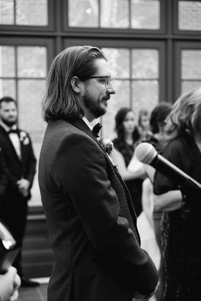 the groom looks down the aisle at his bride during their royal park hotel wedding photos