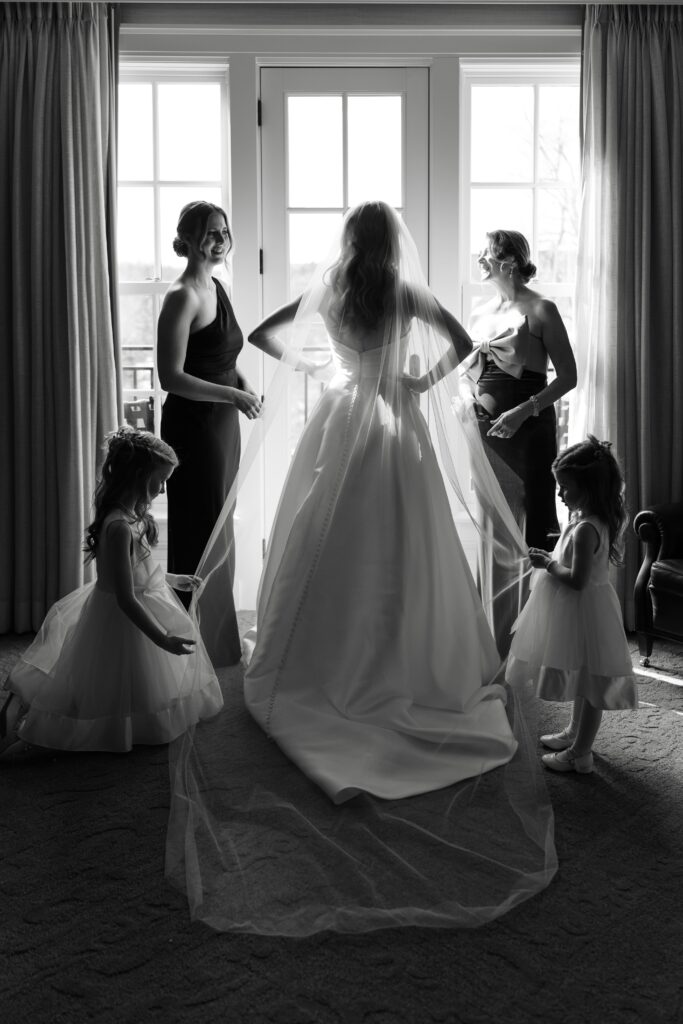 the bride's mother and maid of honor help her get ready with the flower girls