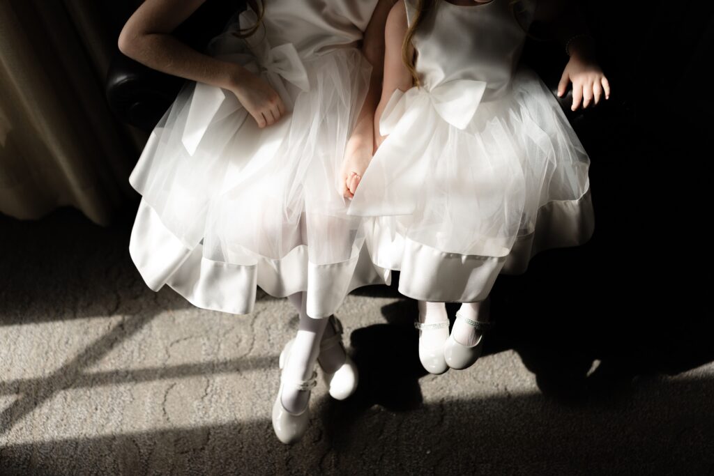 the flower girls sit together in matching white dresses