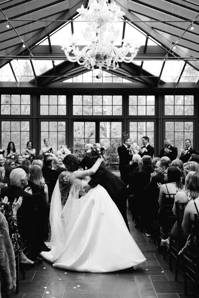 the bride and groom share a kiss halfway down the aisle at their royal park hotel wedding in michigan