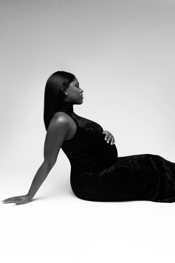 camille leans on her arm behind her as she sits on the ground at her studio maternity photoshoot