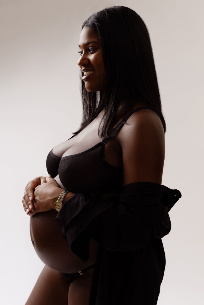 camille smiles as she rests her hands on her belly during her studio maternity photoshoot