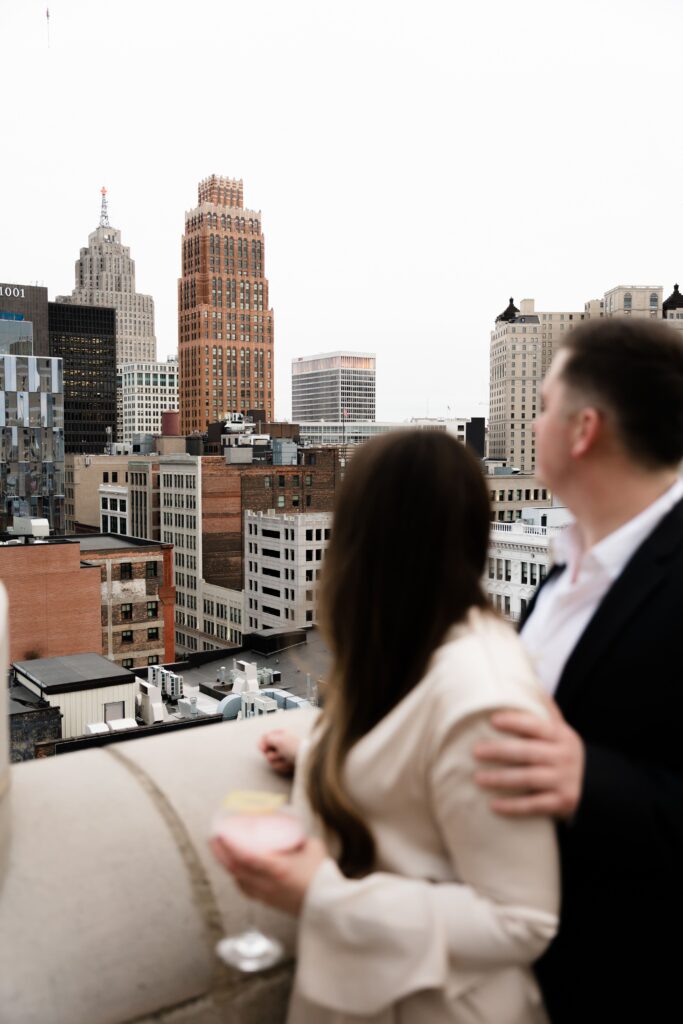 the detroit skyline is in focus as jane and john look out on it