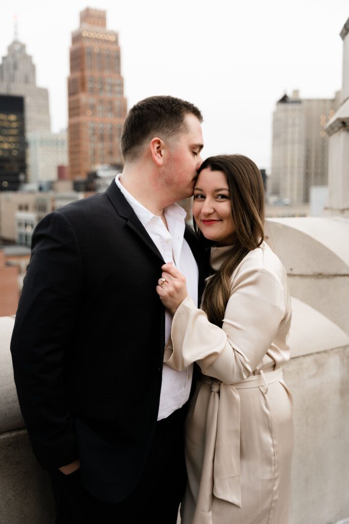 jane smiles as john presses a kiss to the top of her head during their detroit engagement photos