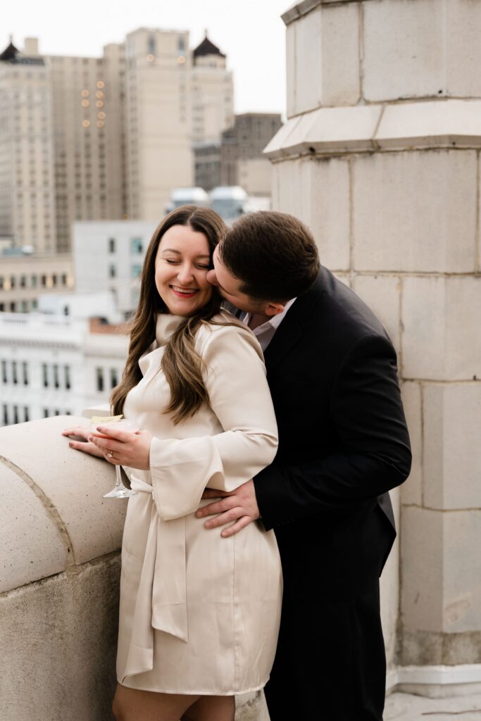 jane smiles at john as he kisses her cheek during their detroit engagement photos