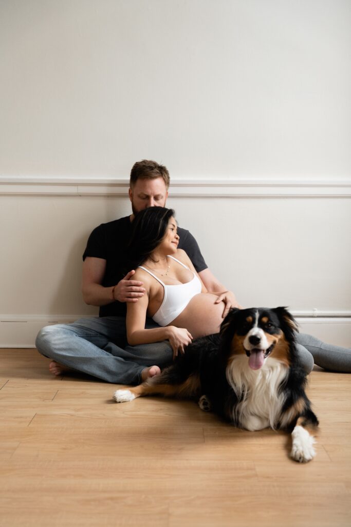 andy presses a kiss to nats head as they sit on the ground with their dog during lifestyle maternity photos