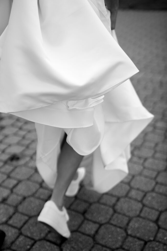 the bride's train is bunched up and carried as she walks in her wedding day sneakers