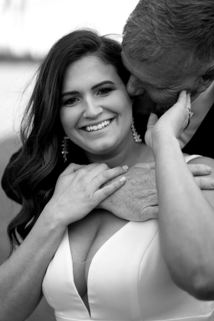 the bride smiles as the groom nuzzles into the side of her face