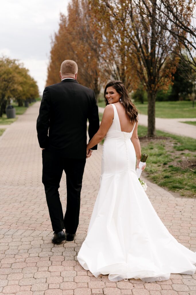 the bride looks back over her shoulder at their michigan elopement photographer while walking hand in hand with the groom