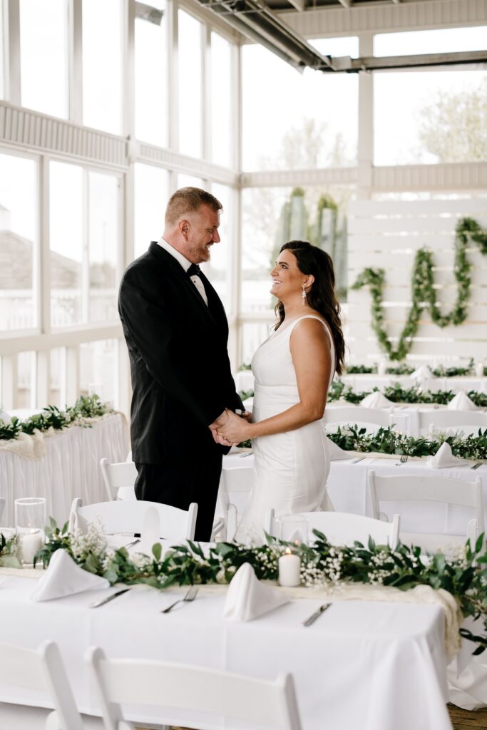 the bride and groom smile at each other while standing between tables at their intimate elopement